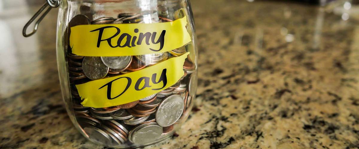 Rainy Day Money Jar. A clear glass jar filed with coins and bills, saving money. The words 