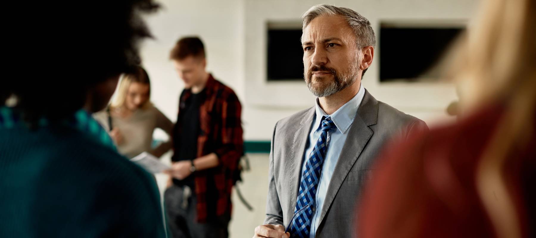 Mature teacher talking to his students in a hallway at the university.