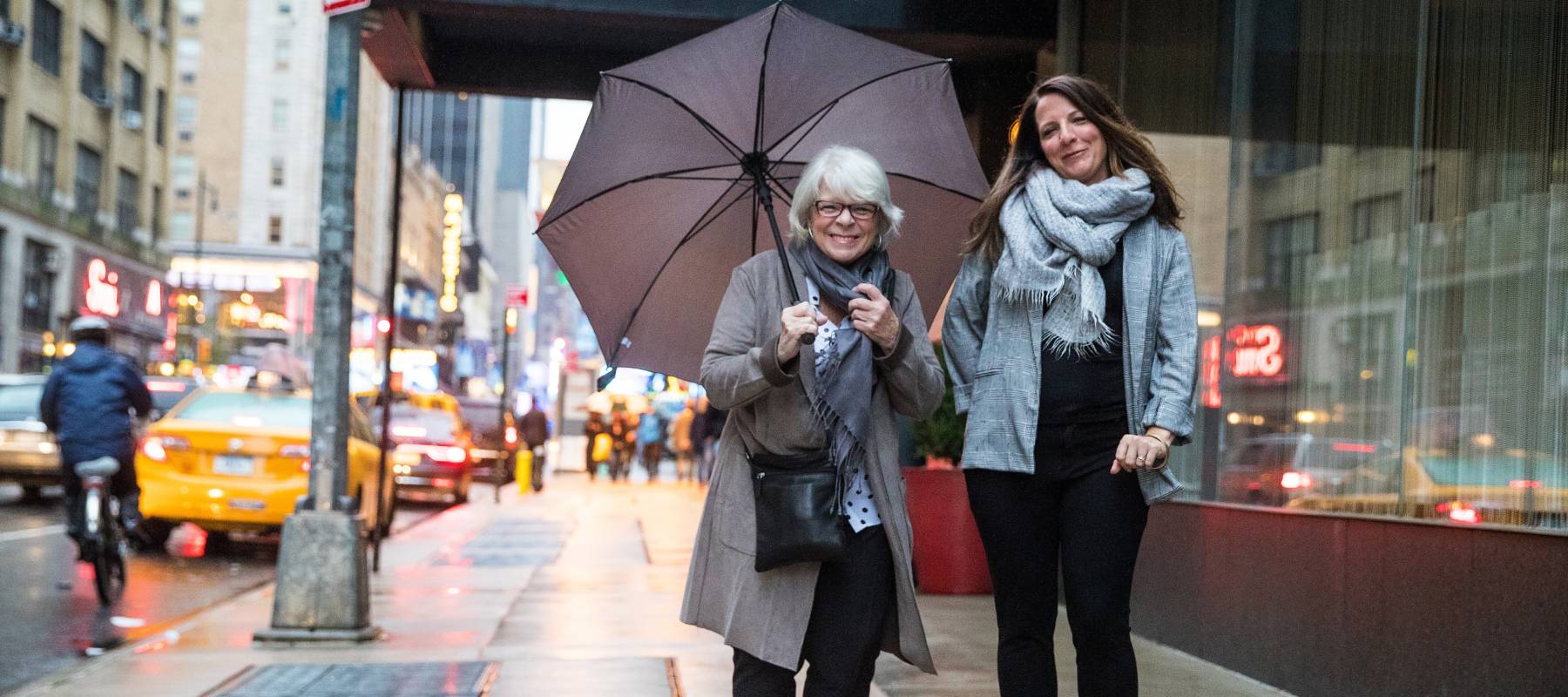 Two women standing on New York sidewalk with umbrella