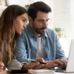 Focused young couple calculating bills, discussing planning budget together, serious wife and husband looking at laptop screen, using online banking services and calculator, checking finances