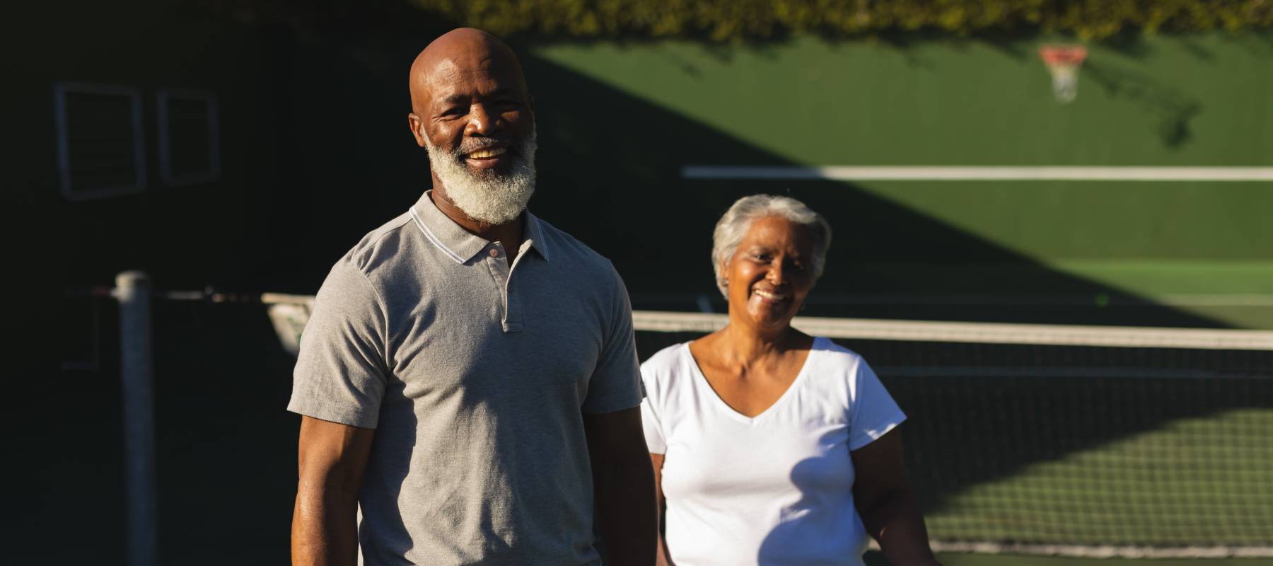 Portrait of smiling senior African American couple with tennis rackets on tennis court.