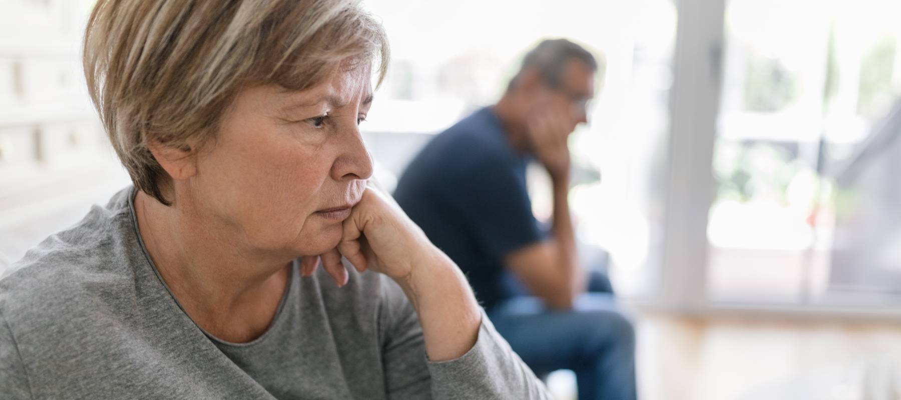 Older woman leaning on hand with man in background