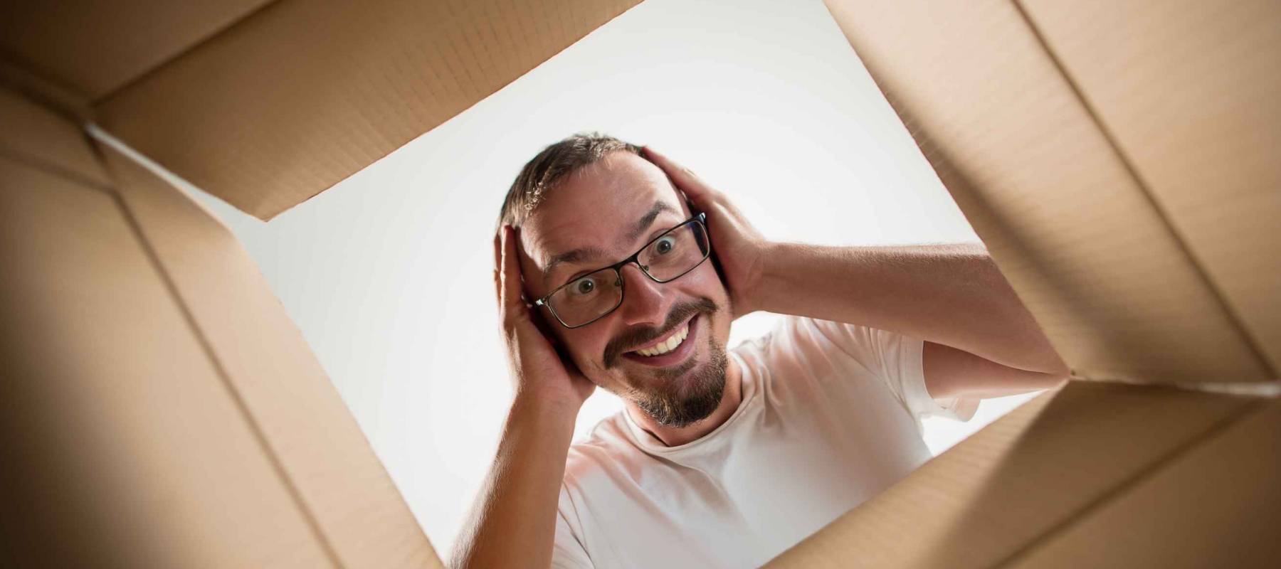 The surprised man unpacking, opening carton box and looking inside. The package, delivery, surprise, gift lifestyle concept. Human emotions and facial expressions concepts