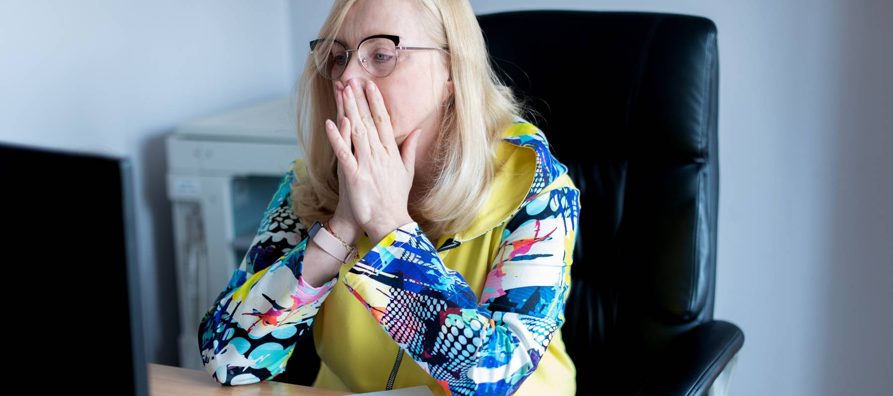 Woman sitting at desk in front of computer with her hands over her  mouth.