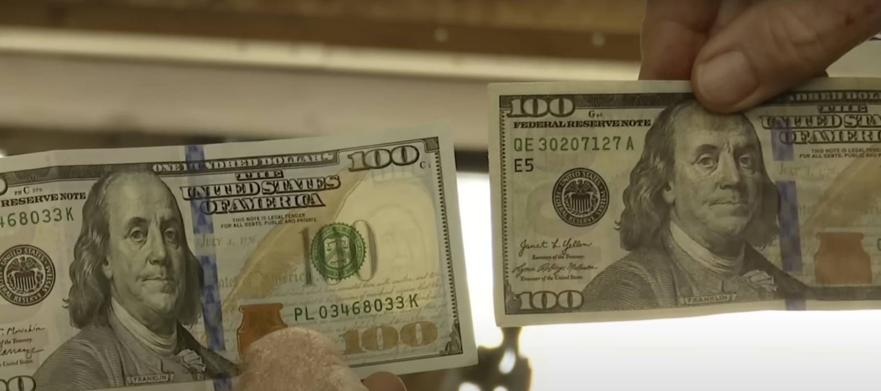 Hands holding a real $100 and a counterfeit $100 made from $1.