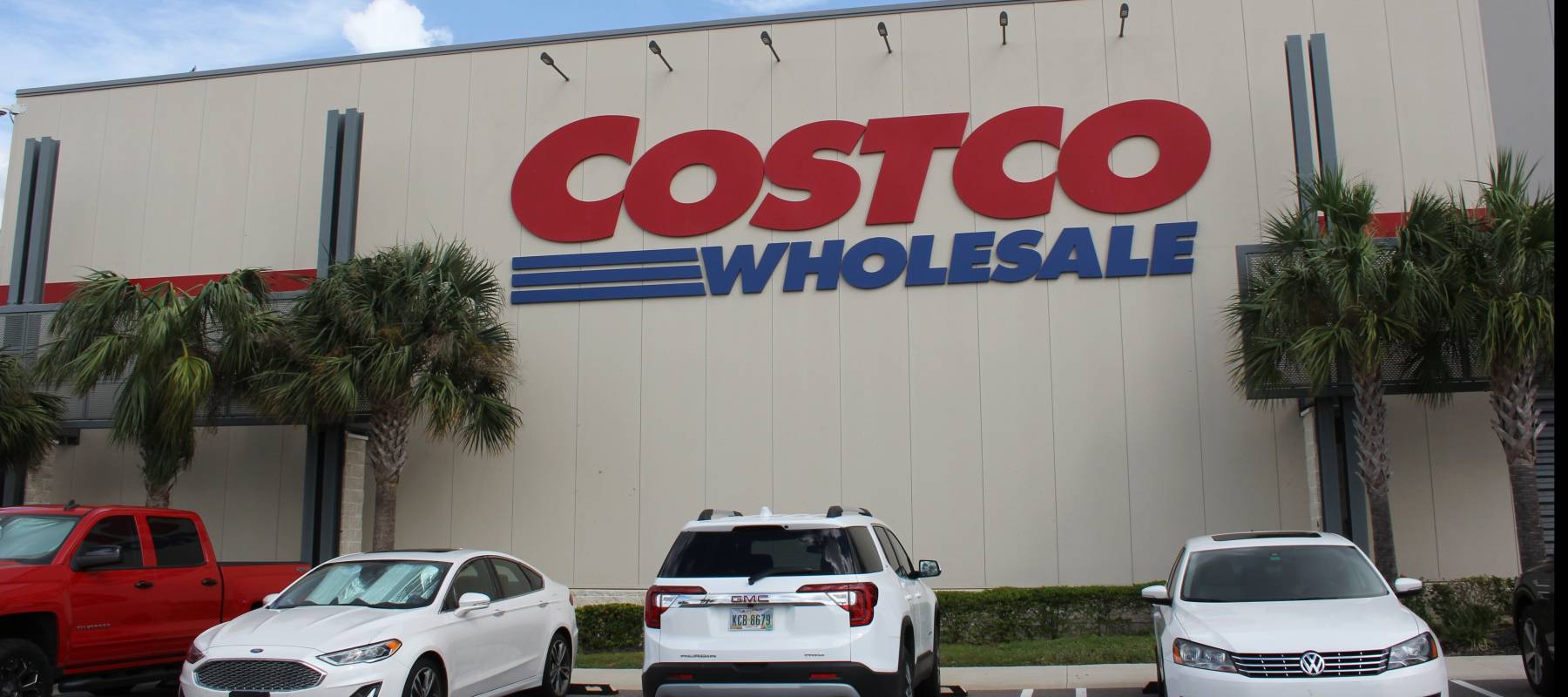 Exterior view of Costco warehouse with cars parked out front and palm trees.
