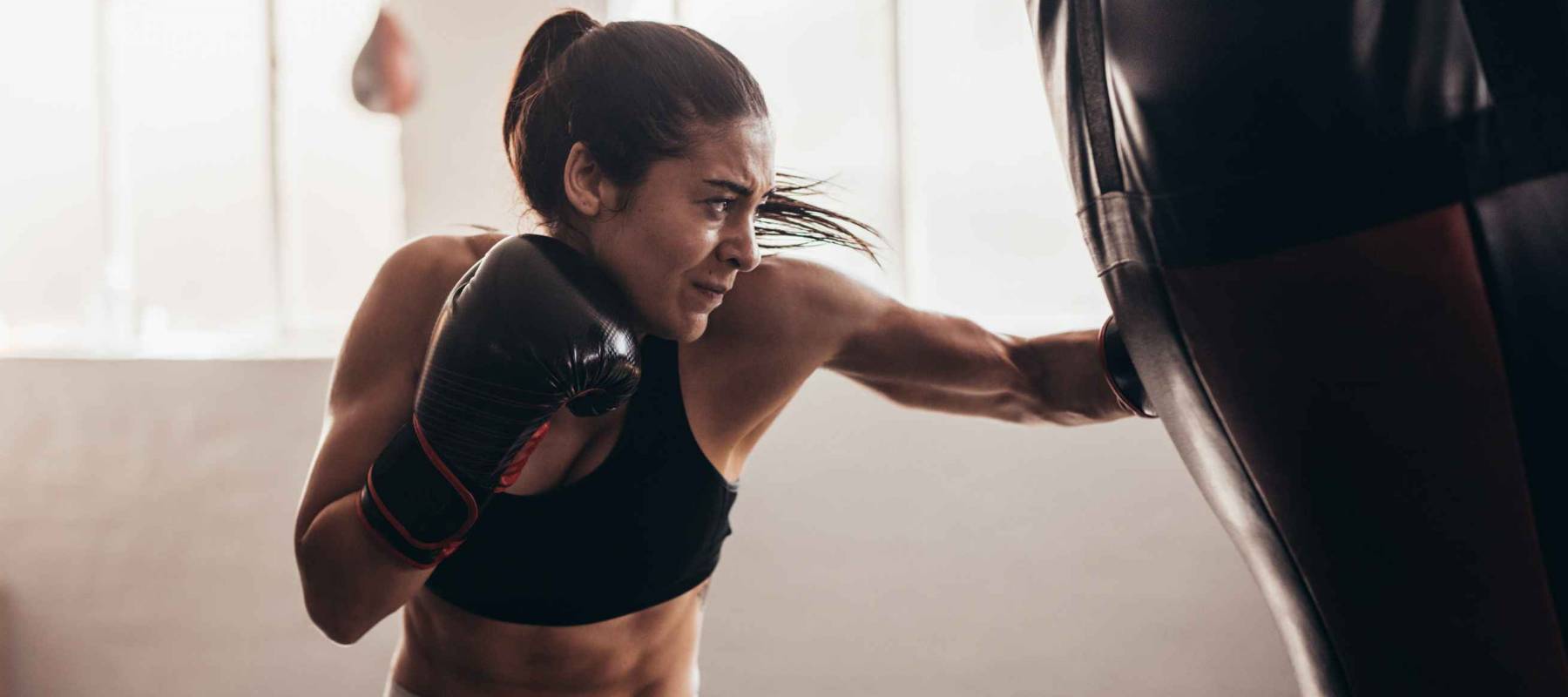 Female boxer hitting a huge punching bag at a boxing studio. Woman boxer training hard.