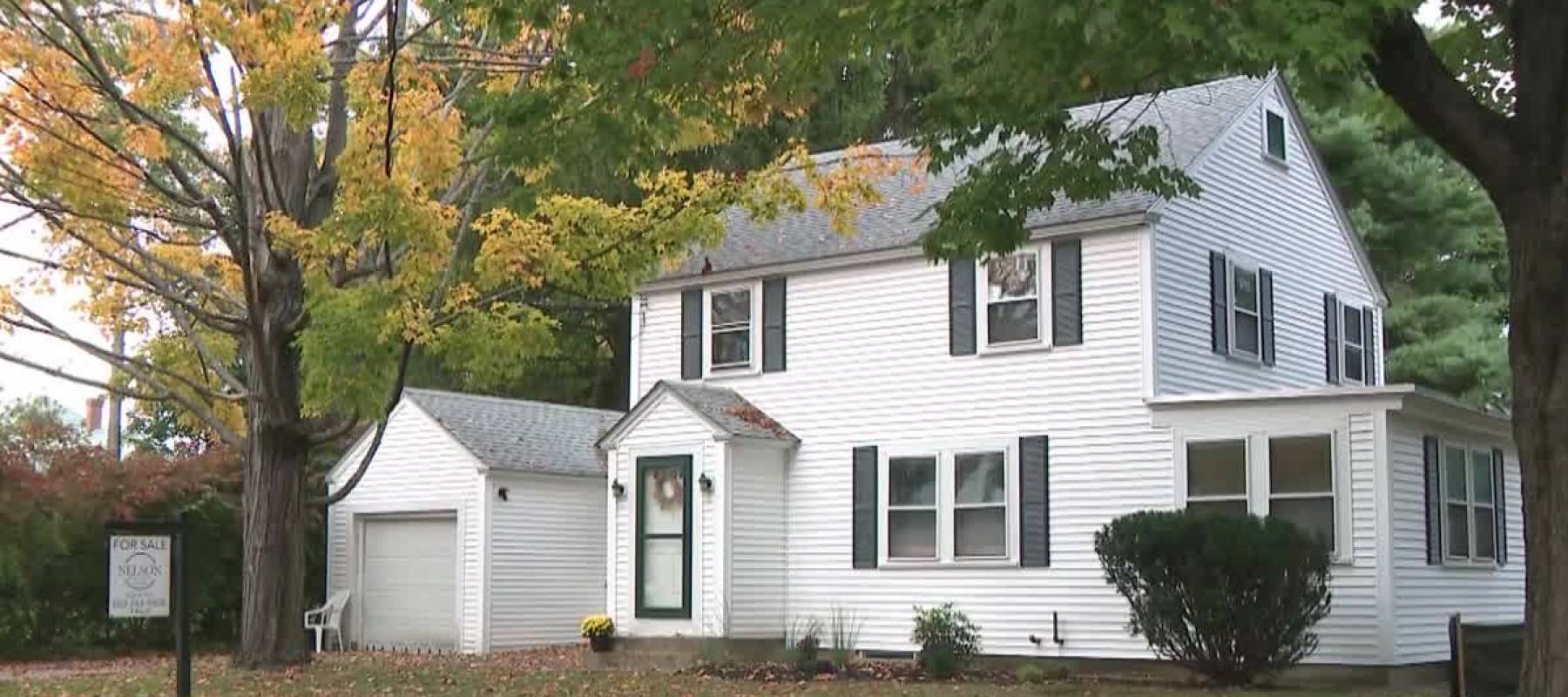 White two-storey clapboard siding house alongside trees with leaves that are turning yellow.
