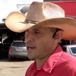 Man in cowboy hat talking on camera, person kneeling by car (inset).