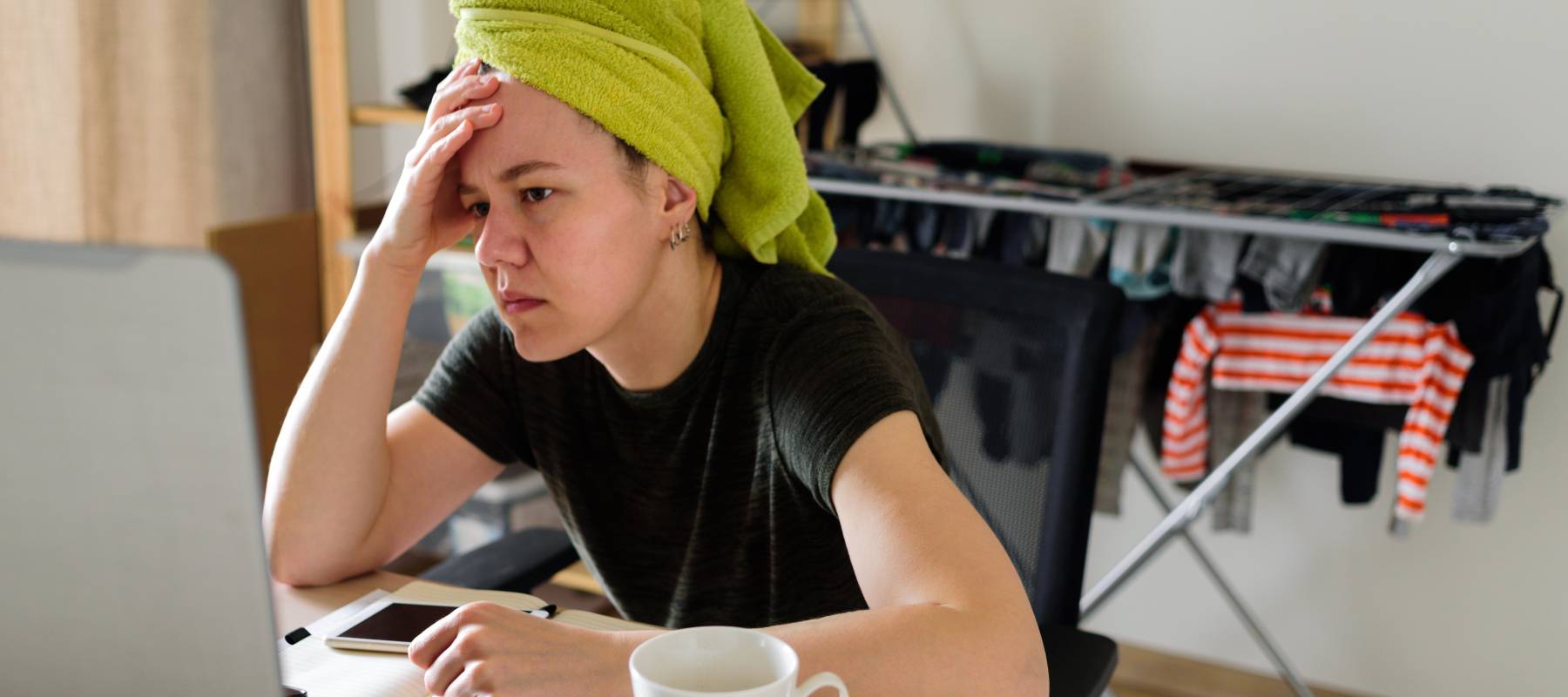 Woman with her hair wrapped in a green towel looking at her computer with a worried expression on her face.