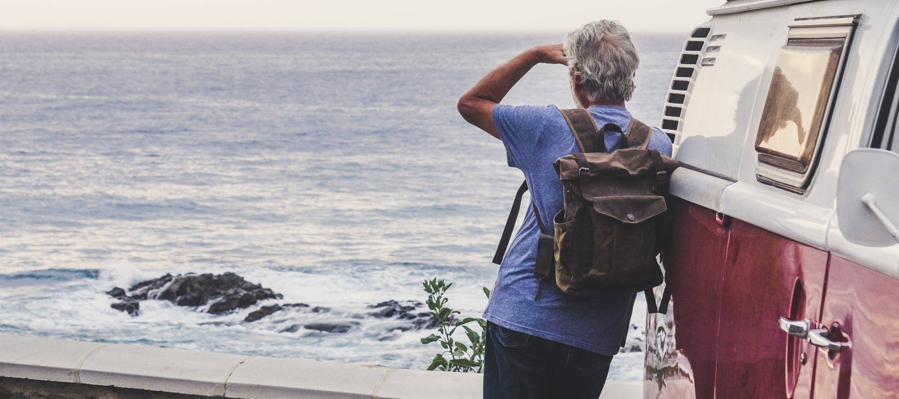 Senior man travelling in a vinatge van, looking at the sea, rear view