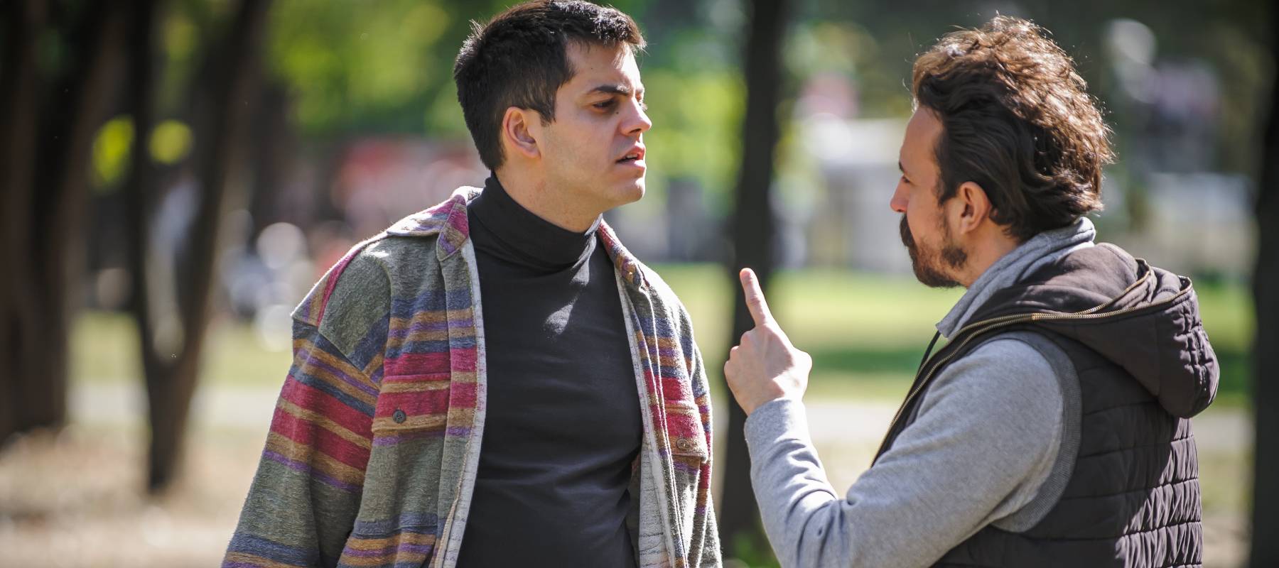 Two middle-aged men arguing with trees in soft focus in the background.