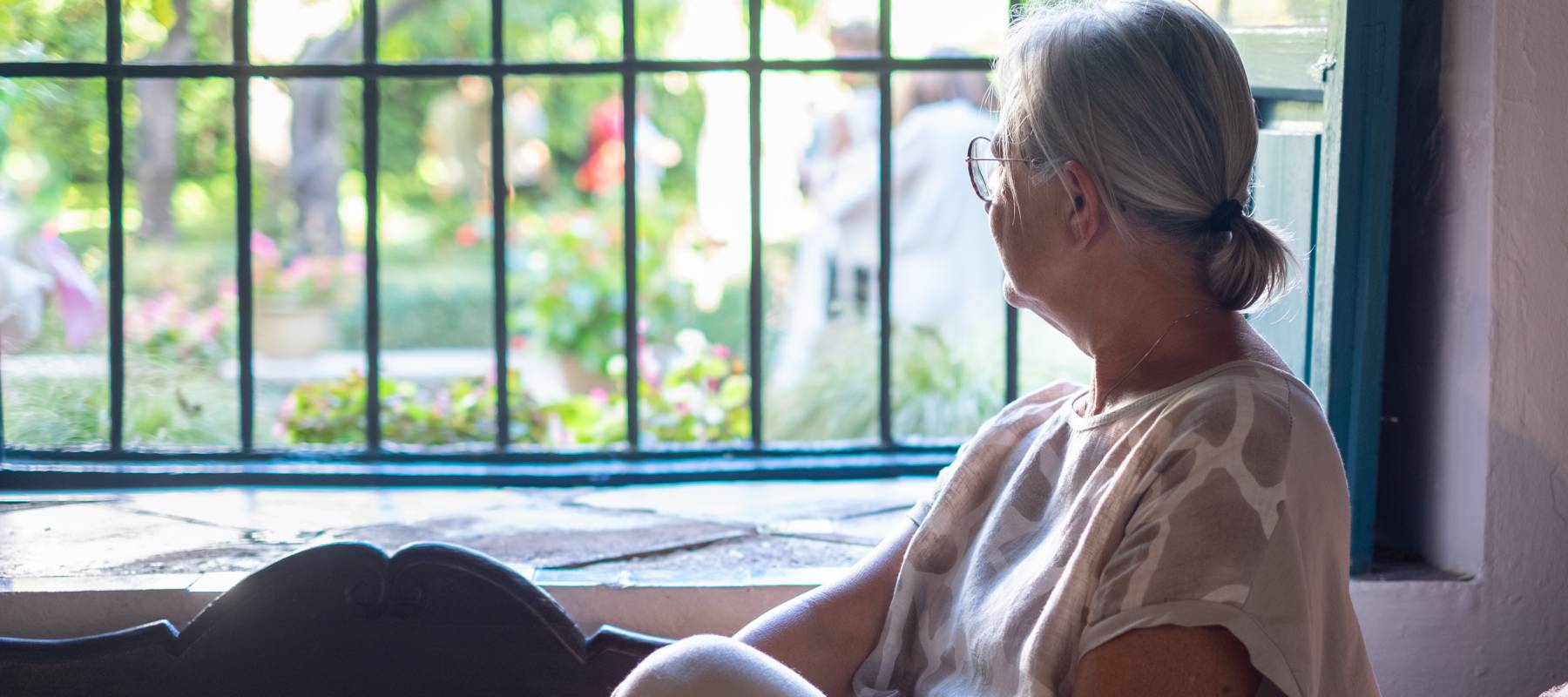 Older woman sitting on a couch, looking out he window.