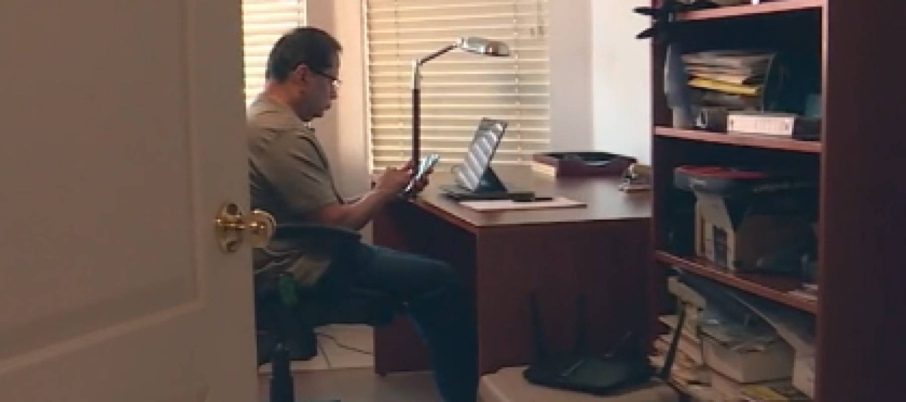 Man sits at a desk behind a laptop.