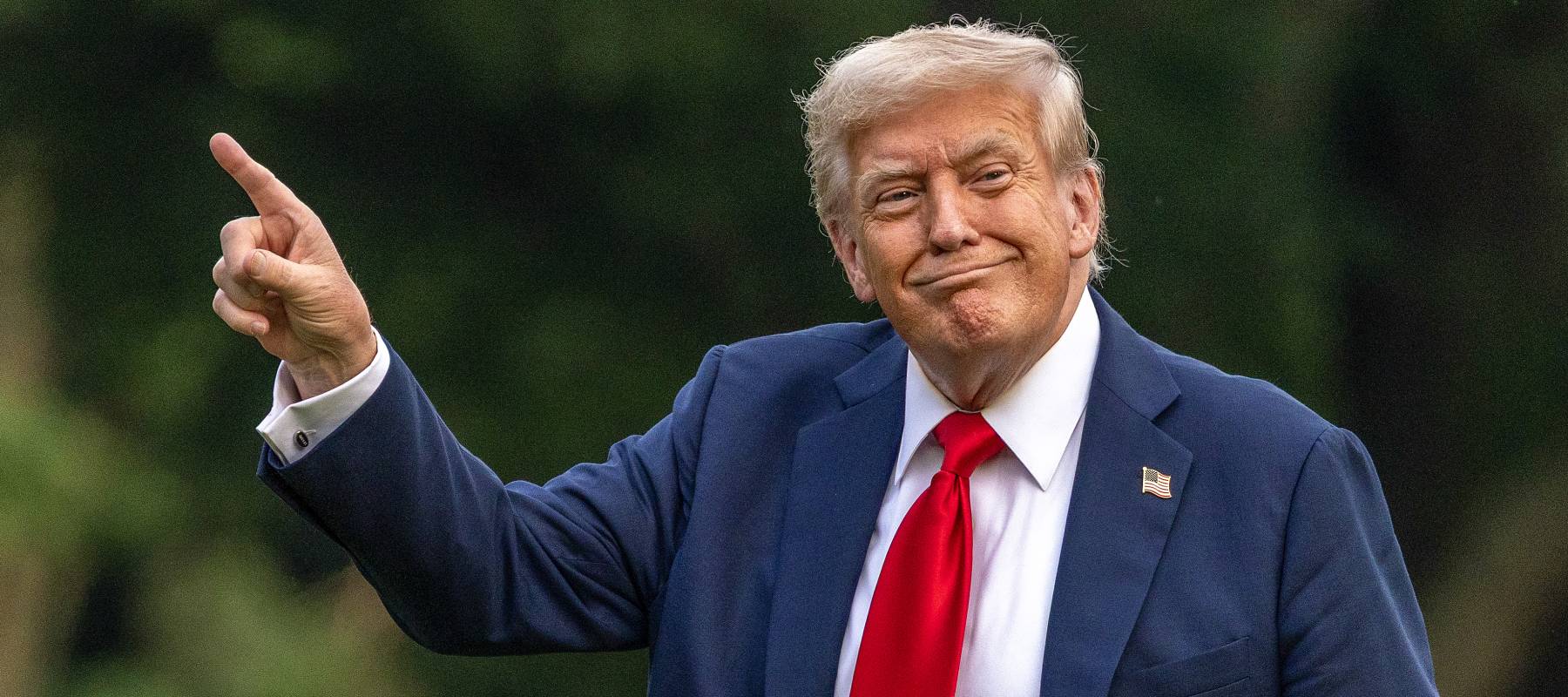 Donald Trump holds up a single finger and points towards the top left of the frame.