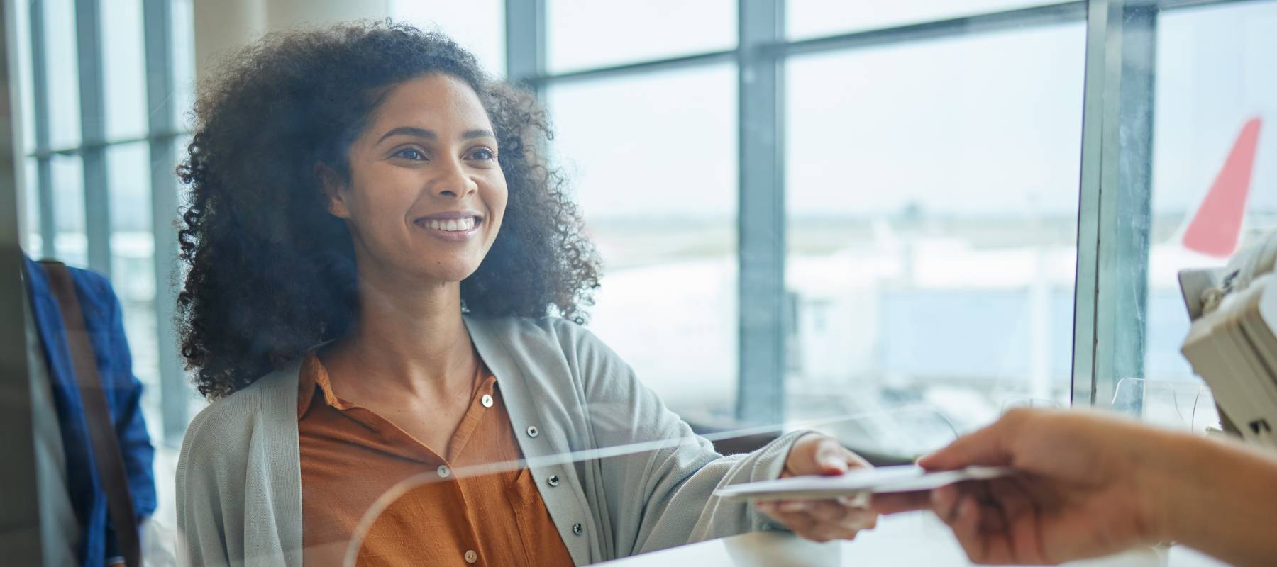 Woman looking through a counter glass optimistically and smiling broadly.