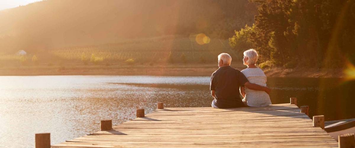 Romantic Senior Couple Sitting On Wooden Jetty By Lake