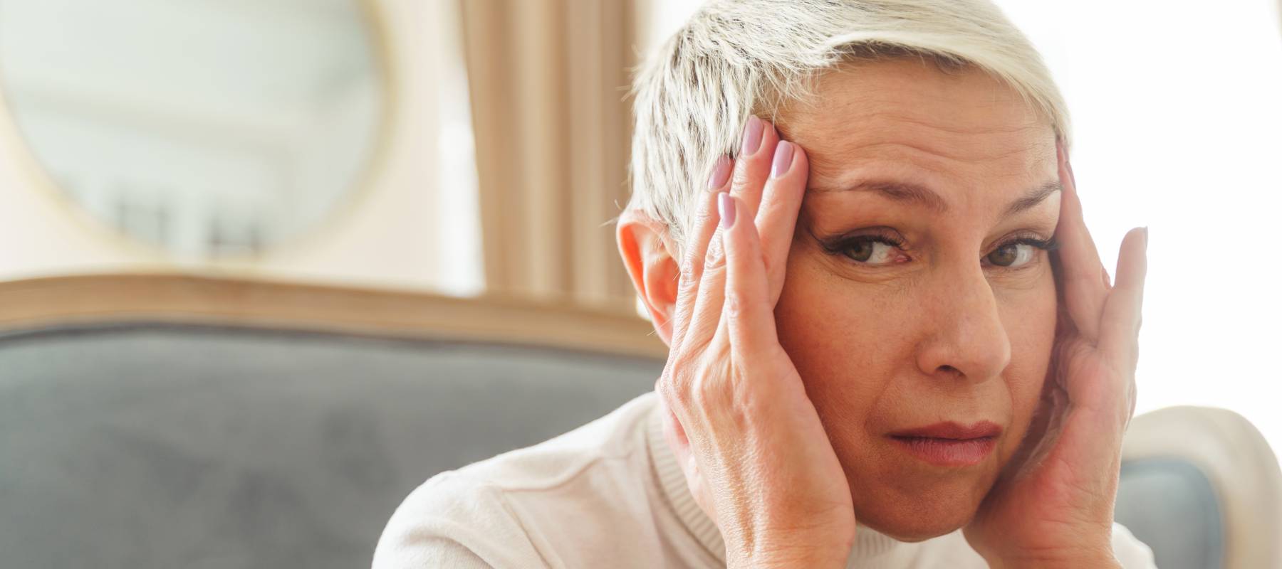 Woman with short white hair holding her temples and looking worriedly at the camera out of the corners of her eyes.
