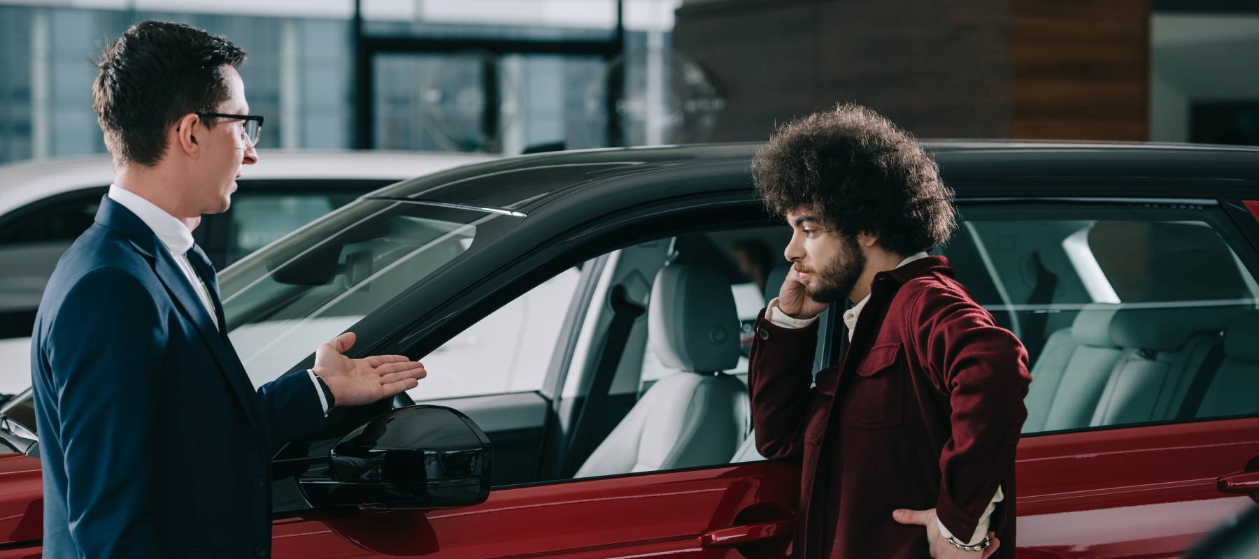 car dealer showing red automobile to curly man