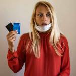 A blond girl wears a protective medical mask, holds a credit card, on a beige background. The concept of quarantine, coronavirus, shopping. shock, credit, no have money, work after quarantine