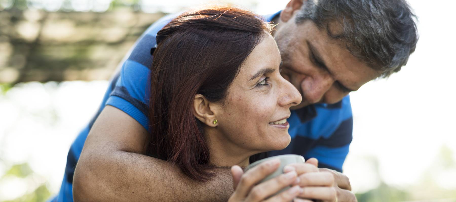 A man hugs a woman holding a cup.
