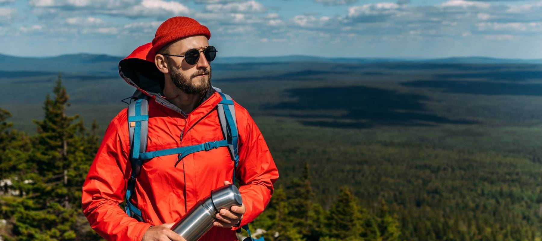 A bearded traveler with a backpack on the top of a mountain