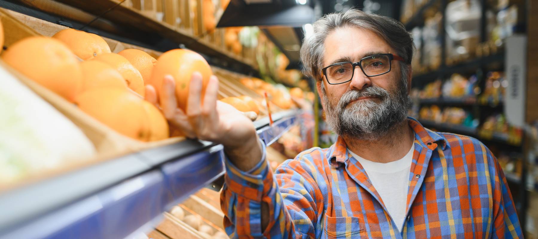 Gentleman with salt-and-pepper hair reaching for an orange at a grocery store.