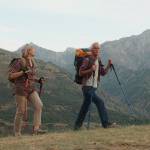 An older couple hike across a rise with mountains in the distance.