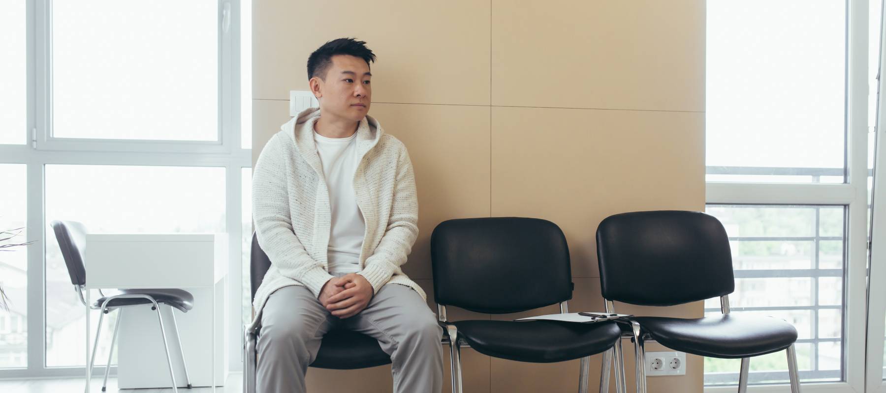 Middle-aged man waiting for an appointment on a black waiting room chair.