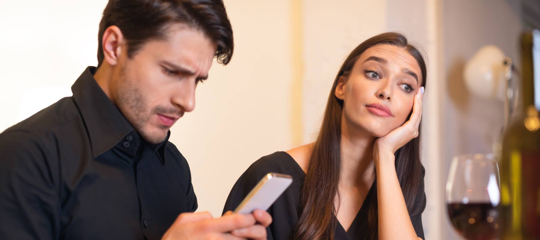Young man looking worriedly at his phone while the woman he's with stares off into the distance bored and distracted.