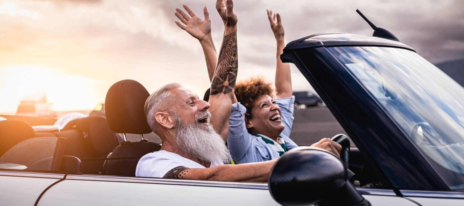 a stylish boomer couple raising their arms and smiling in a luxury car