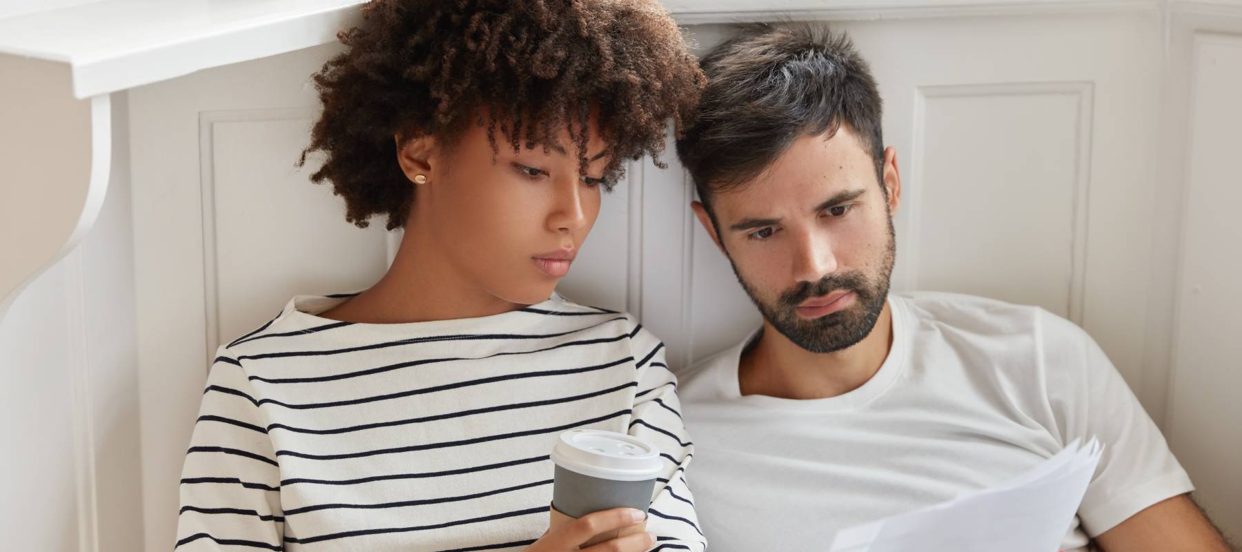 Couple sitting next to each other and looking at papers with serious expressions.