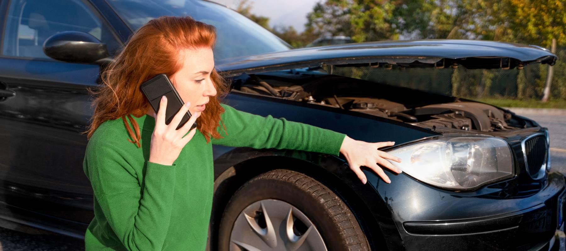Woman crouching and examining the bumper of her car.