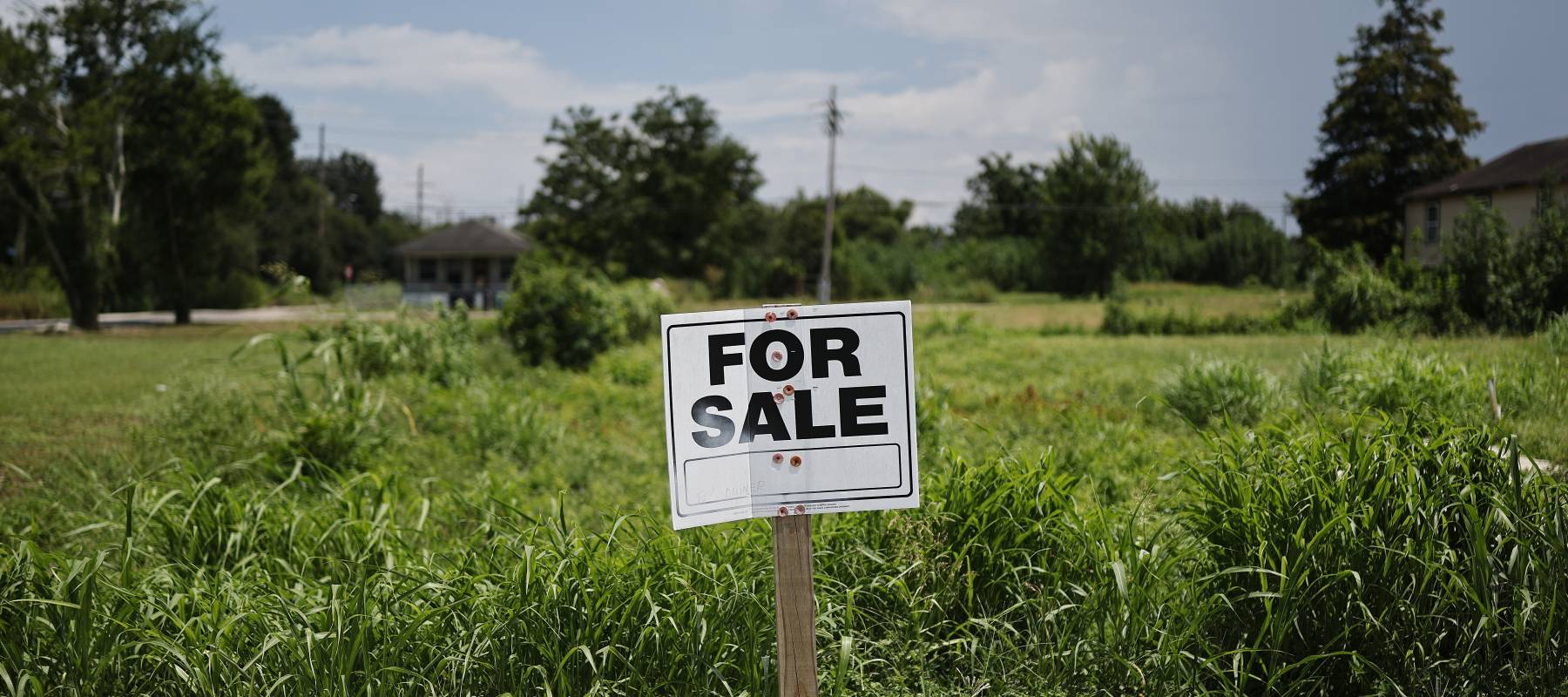 A 'For Sale' sign is posted on a vacant lot.