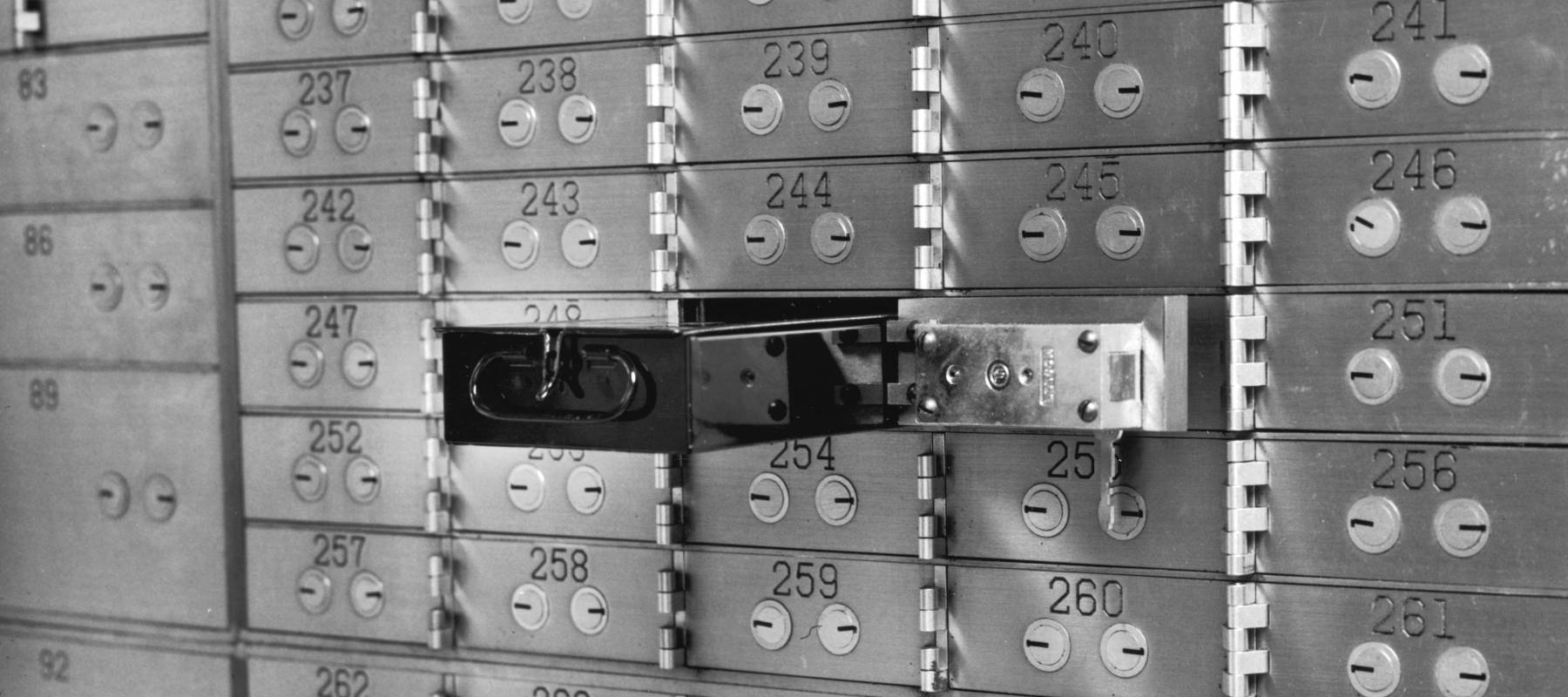 An open bank safety deposit box in a wall of numbered boxes with key holes.