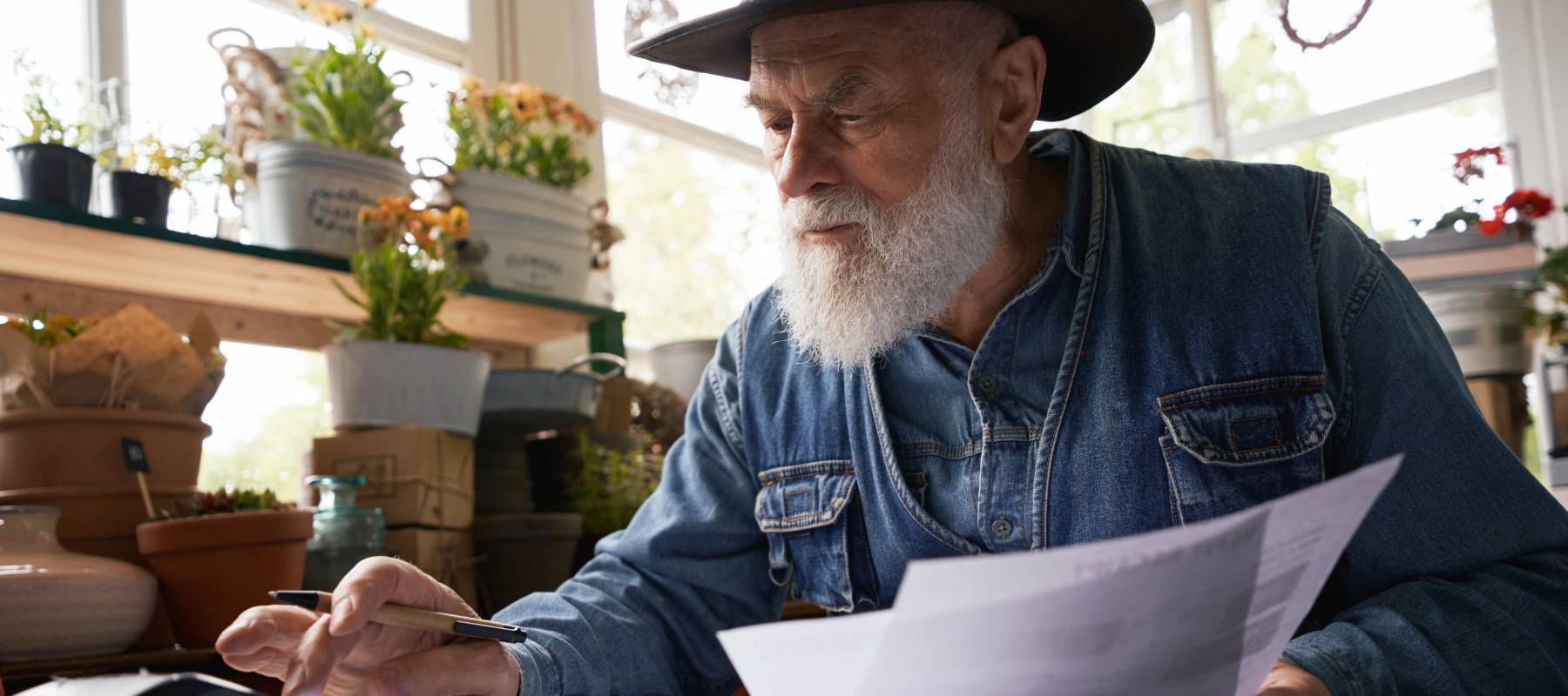 older Caucasian man holding pieces of paper and using a calculator at home