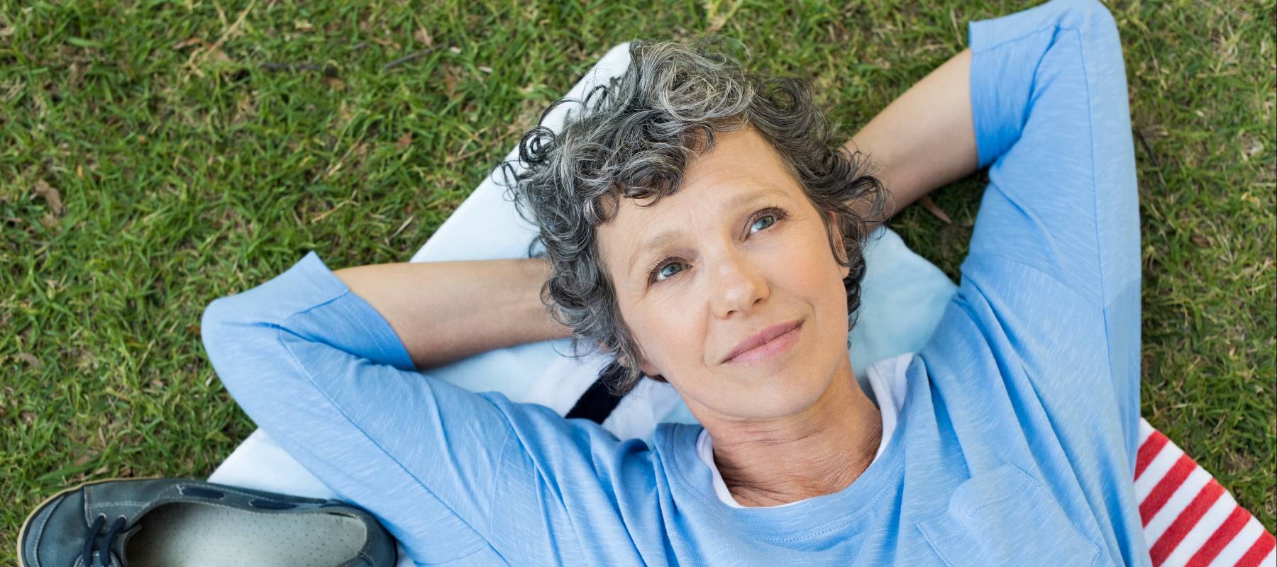 Pensive woman lying on towel on grass.