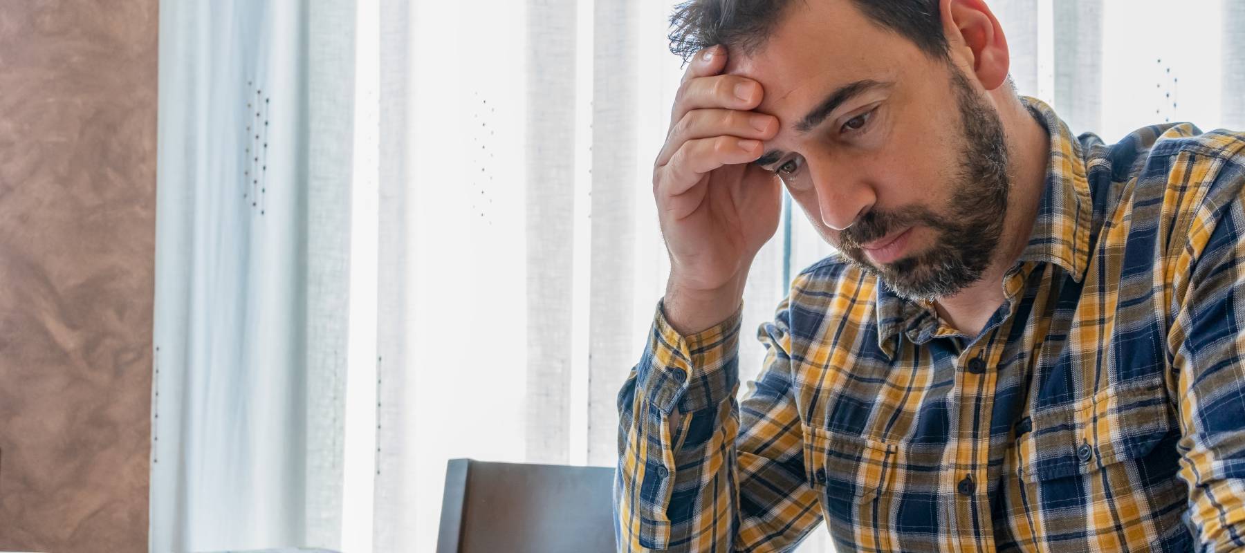 Bearded 40-something man dressed in plaid shirt looking at bills and worried.