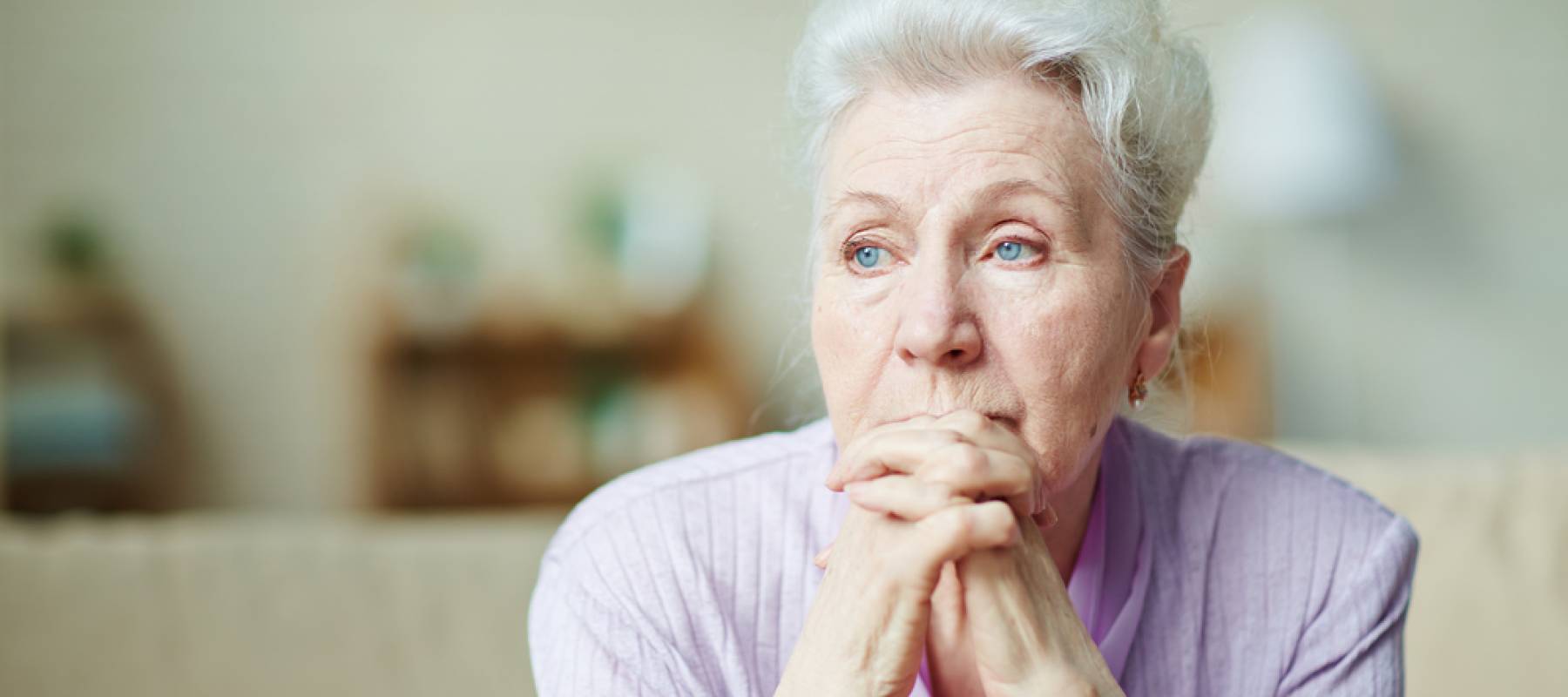 Caucasian senior woman sitting on couch, looking sad