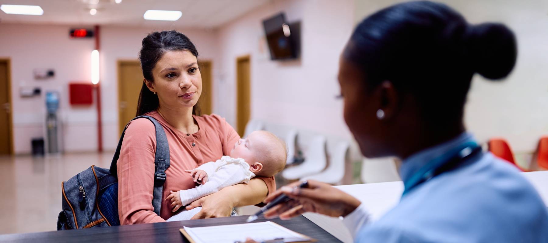 A mother holds her baby while speaking with a nurse at a hospital.