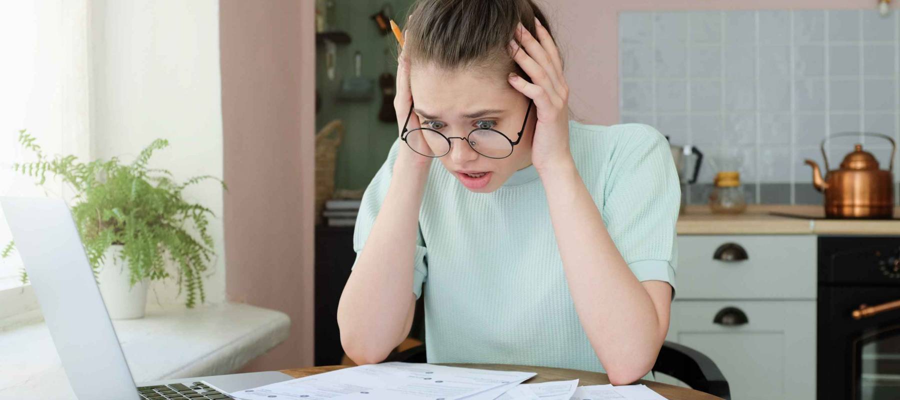 Young anxious worrying woman looks desperately to bills, faces problems with paying taxes, holding head with both hands