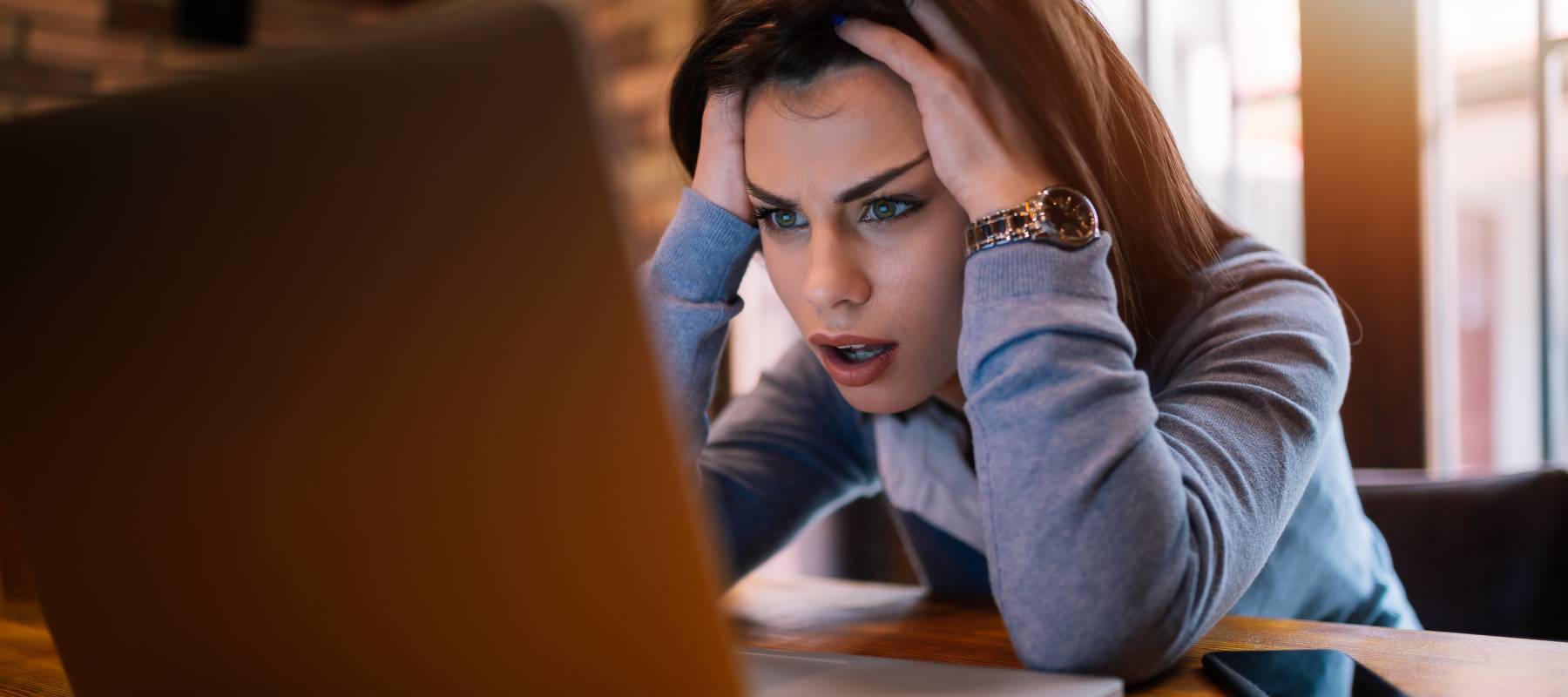 Woman holding her head as she looks at laptop.