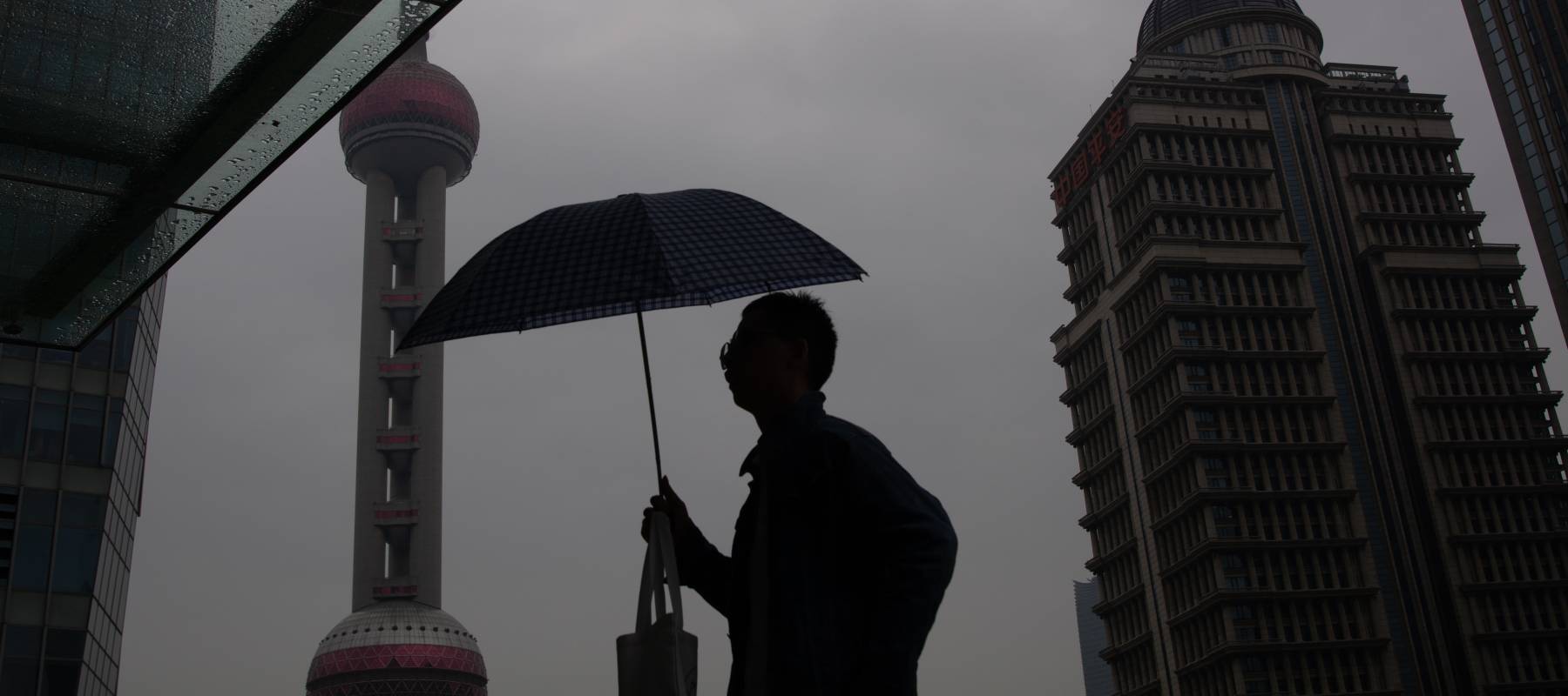 A man is walking with an umbrella as the Oriental Pearl TV Tower is seen in the background in Shanghai, China