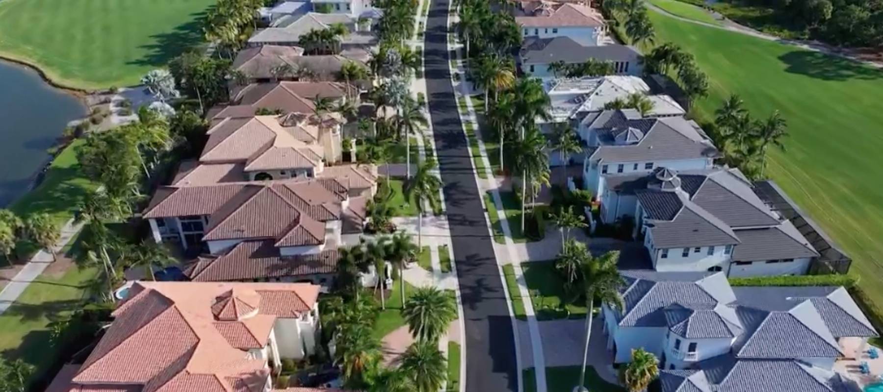 Aerial view of gated community with golf course, palm trees, and lake.
