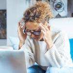 woman at home in front of laptop touching head temples for migraine or stress