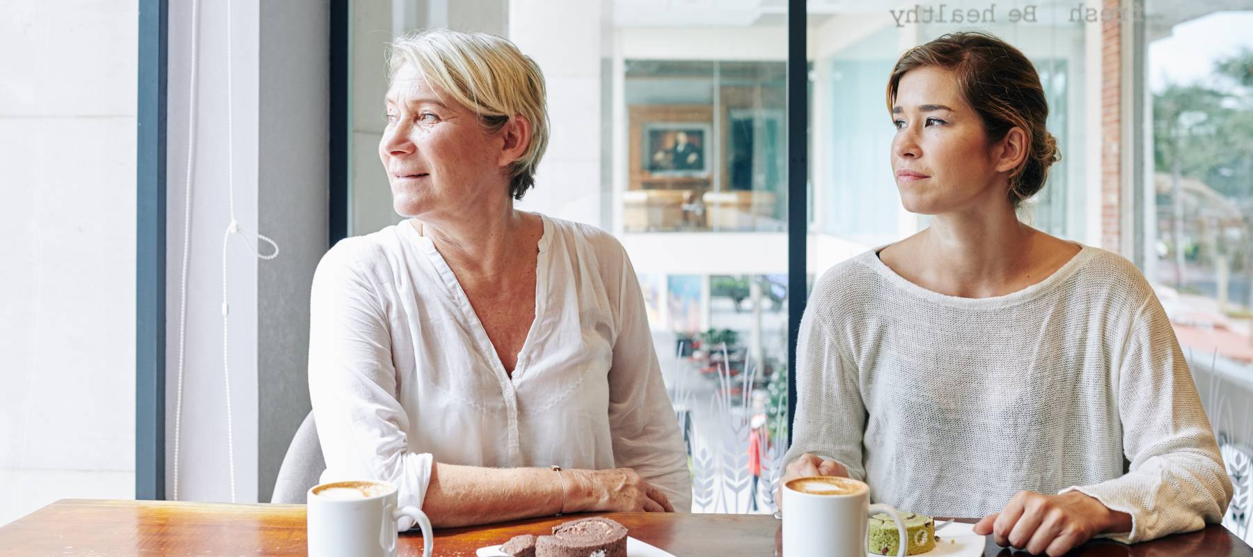 A mother and daughter sit at a table with coffee.