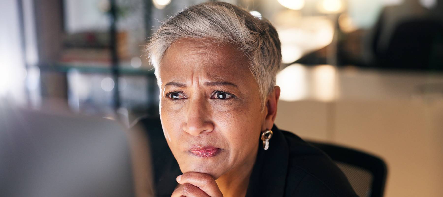 Woman looking at computer screen, stressed out, hand on chin, worried.