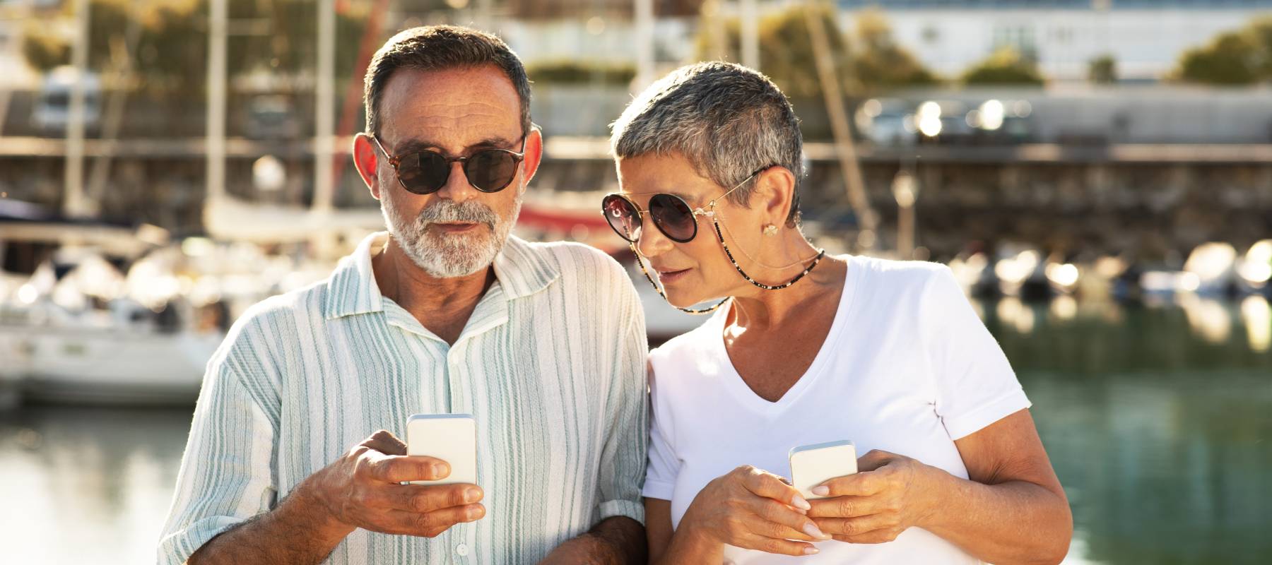Couple looking at their phones at a marina.