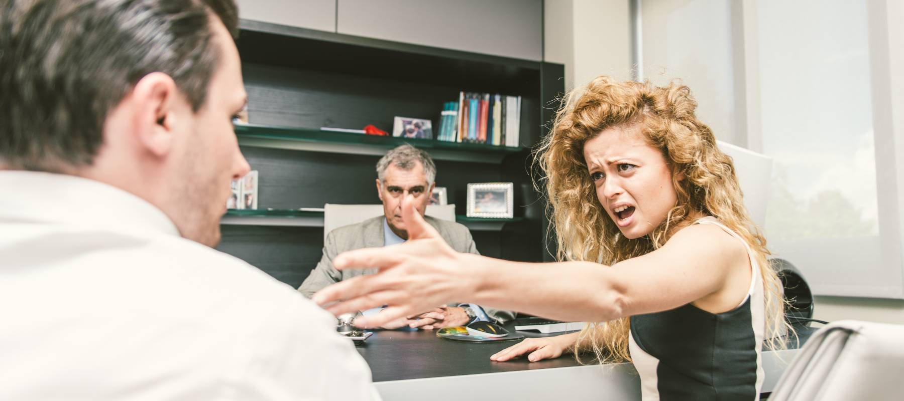 a young Caucasian woman arguing in an office with two men