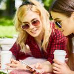 Y-generation girls searching in smartphone and having drinks while relaxing in park